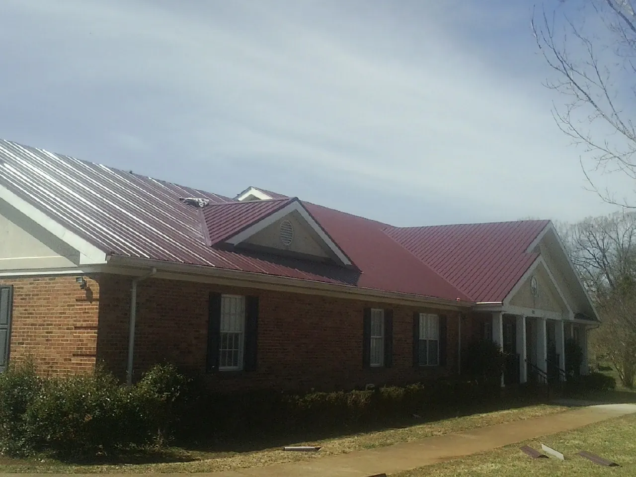 Red metal roof with gabled entries on a long brick building, from a Hail Damage Roof Repair job in Hye