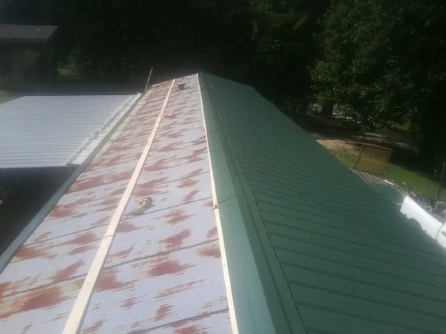Old rusted panels beside newly installed green metal roofing — Wind Damage Roof Repair by Roofing Brothers in Hye