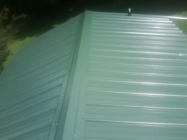 New green metal panels meeting at the ridge of a roof — Flat Roof Repair work by our crew in Hye