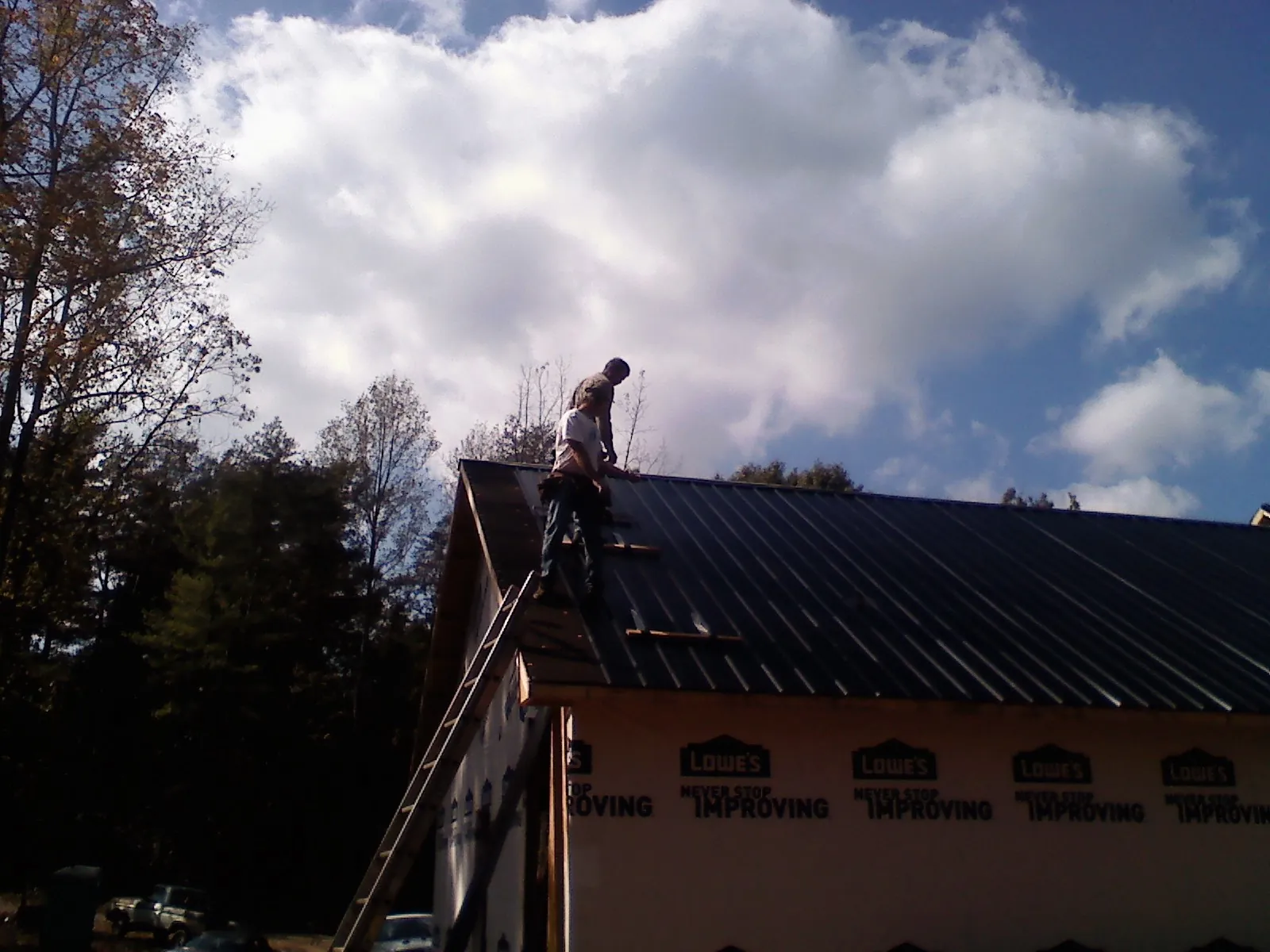 Roofer fastening dark metal panels high against a cloudy sky, from a Roof Inspection job in Hye
