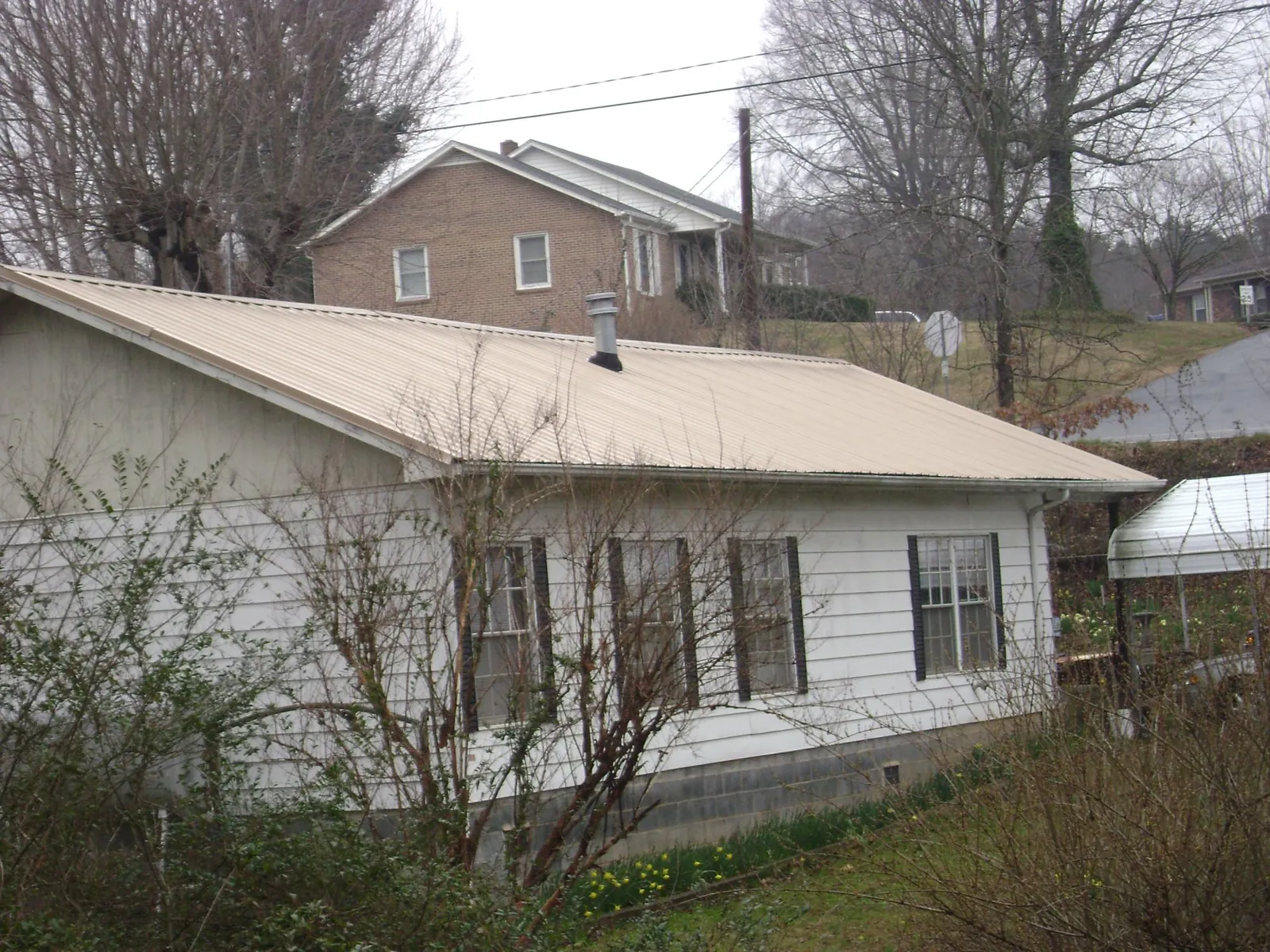 Tan metal roof on a white sided house set into a hillside — Commercial Roofing by Roofing Brothers in Hye