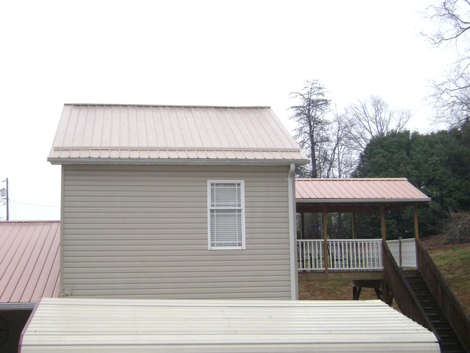 Tan metal roofs on a two story addition and attached porch, from a Roof Replacement job in Hye